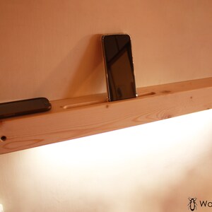 May include: A wooden shelf with a built-in phone holder and a light fixture. Two cell phones are resting on the shelf.