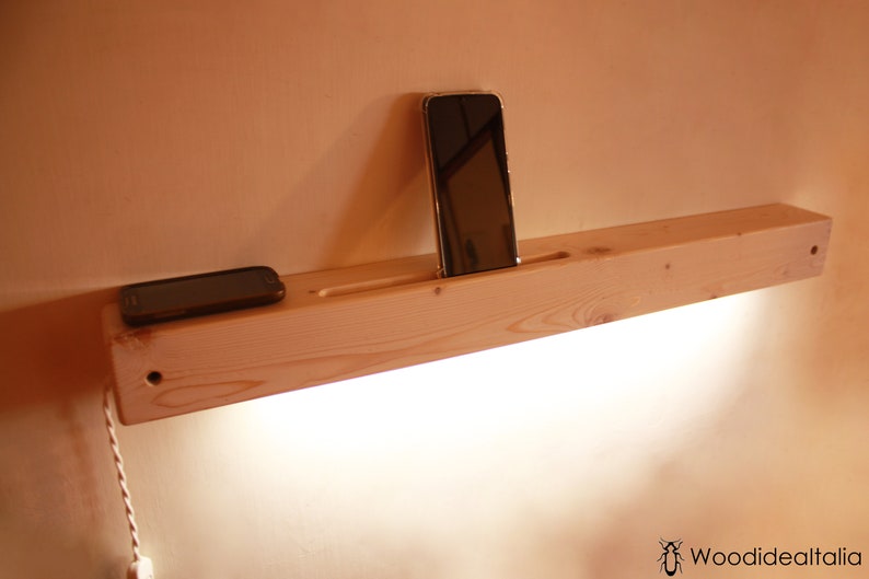 May include: A wooden shelf with a built-in phone holder and a light fixture. Two cell phones are resting on the shelf.