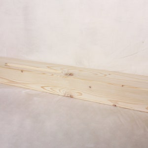 May include: A long, rectangular wooden box with a white cord attached. The box is made of light-colored wood and has a smooth finish.