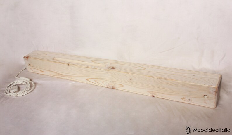May include: A long, rectangular wooden box with a white cord attached. The box is made of light-colored wood and has a smooth finish.