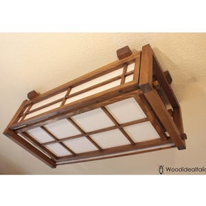 May include: A rectangular wooden ceiling light fixture with a grid design and white panels. The fixture is made of dark brown wood and is mounted on a light-colored ceiling. The overall design is reminiscent of Japanese style.