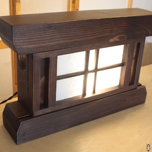 Op de afbeelding: Een donkerbruine houten lamp met een matglas venster. De lamp heeft een eenvoudig, traditioneel ontwerp en wordt van binnenuit verlicht.