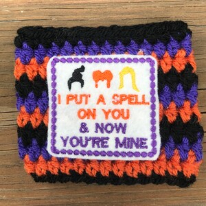 May include: A black, orange, and purple crocheted wrist cuff with an embroidered patch that says "I put a spell on you & now you're mine".