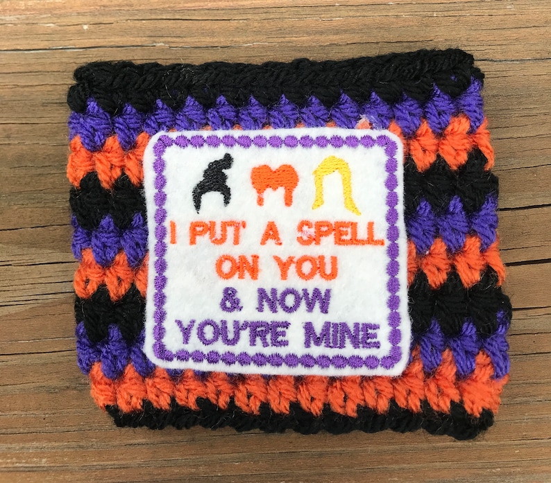 May include: A black, orange, and purple crocheted wrist cuff with an embroidered patch that says "I put a spell on you & now you're mine".