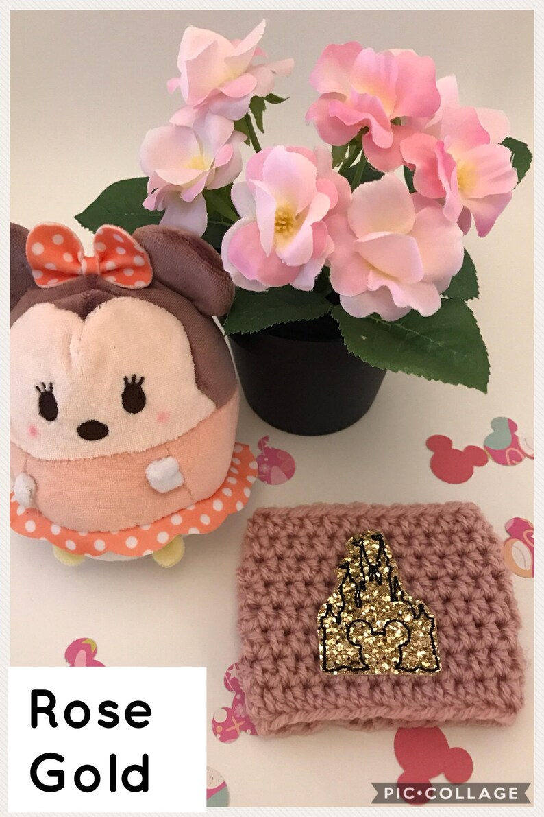 May include: A pink crocheted coffee cup cozy with a gold glitter castle design. The text "Rose Gold" is written below the cozy.