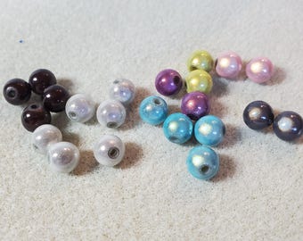 May include: A collection of colorful, round beads in various shades including brown, silver, blue, purple, yellow, and pink. The beads have a glossy finish and are scattered on a light-colored surface, suitable for jewelry making or crafts.