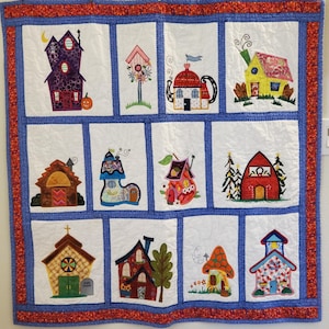 Puede incluir: Un edredón caprichoso con doce diseños de casas bordadas. Cada casa es única, con diferentes colores y estilos, incluyendo una casa embrujada morada, una casa tetera y una casa hongo. El edredón tiene un borde azul con un ribete rojo.