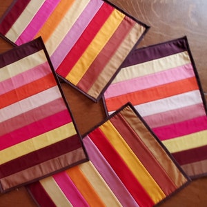 May include: Four colorful striped placemats with brown trim. The placemats are made of fabric and have a patchwork design.