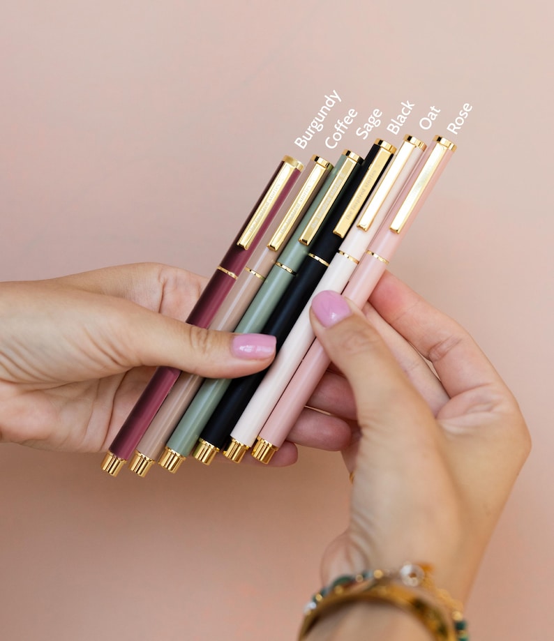 K&ouml;nnte beinhalten: Ein Set aus sechs Stiften mit goldfarbenen Clips und Akzenten, die in einer Reihe angeordnet sind. Die Stifte sind mit den Farben Burgundy, Coffee, Sage, Black, Oat und Rose beschriftet. Jeder Stift hat einen glatten, einfarbigen Schaft.