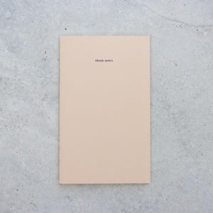 May include: A rectangular notebook with a solid light beige cover. The words blank notes are printed in small, black, lowercase sans-serif font near the top center of the cover. The notebook has a clean, flat, and uniform appearance.