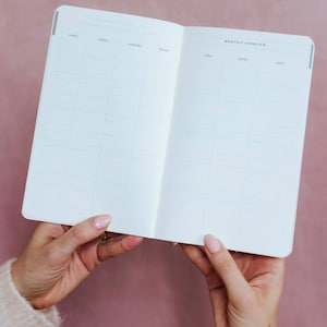 K&ouml;nnte beinhalten: Ein offener Planer mit einer Monats&uuml;bersicht auf wei&szlig;em Papier mit hellgrauen Rasterlinien. Die &Uuml;berschriften umfassen Montag, Dienstag, Mittwoch, Donnerstag, Freitag, Samstag und Sonntag. Der Text Monthly Overview ist oben rechts aufgedruckt.