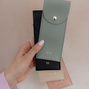 K&ouml;nnte beinhalten: Eine Sammlung von vier rechteckigen Etuis in Salbeigr&uuml;n, Schwarz, Beige und Altrosa. Jedes Etui hat einen goldenen Druckknopfverschluss und eine goldene Schriftpr&auml;gung. Das salbeigr&uuml;ne Etui ist mit D.L., das schwarze mit W., das beige mit MUM und das rosa mit LISA beschriftet.
