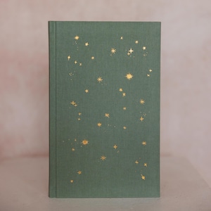 May include: A hardcover journal with a green cover adorned with gold foil star designs. The journal's cover has a textured appearance, and the stars vary in size and arrangement, creating a celestial theme.