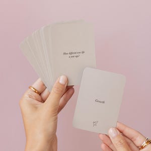 May include: A stack of light beige cards with rounded corners. One card reads "How different was life a year ago?" and another reads "Growth". A small heart symbol is at the bottom of the "Growth" card.