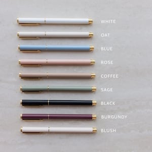 May include: A collection of nine pens arranged horizontally, each featuring a gold-toned clip and tip. The pens are labeled by color: white, oat, blue, rose, coffee, sage, black, burgundy, and blush. Each pen has a smooth, matte-finish barrel.
