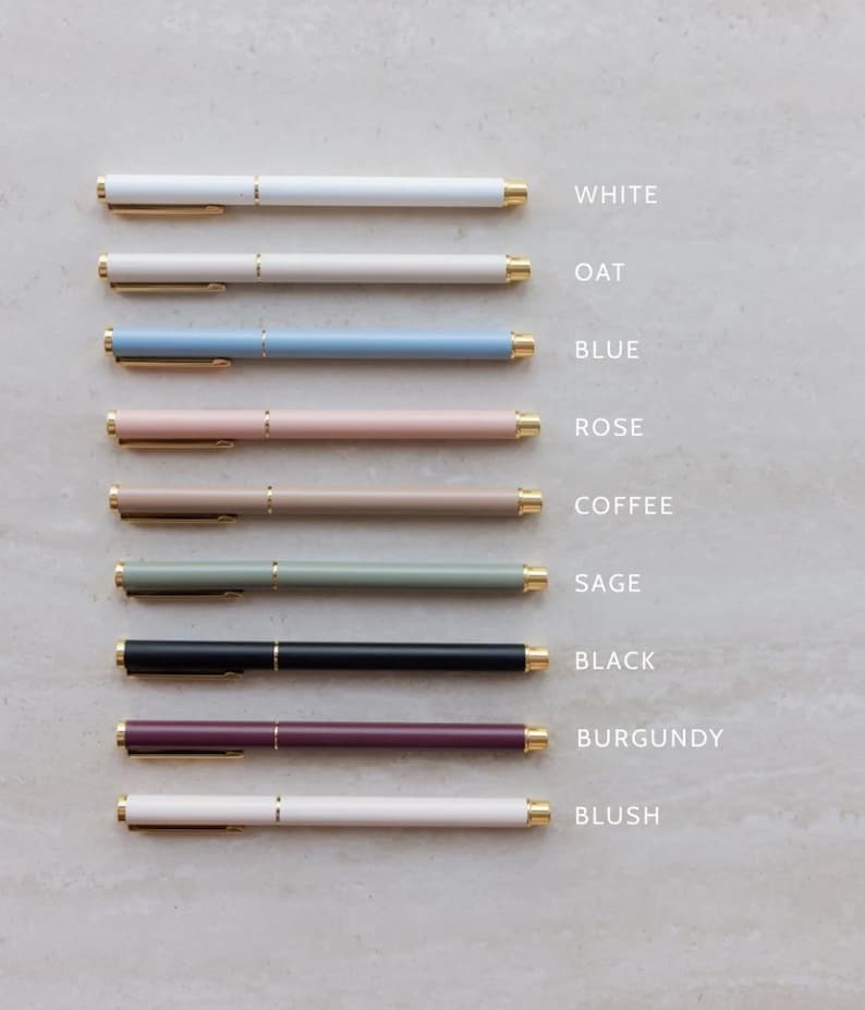 May include: A collection of nine pens arranged horizontally, each featuring a gold-toned clip and tip. The pens are labeled by color: white, oat, blue, rose, coffee, sage, black, burgundy, and blush. Each pen has a smooth, matte-finish barrel.