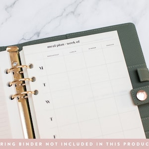 May include: A green planner with gold rings and a white page with the text "meal plan - week of" and columns for breakfast, lunch, dinner, and snacks. The days of the week are labeled M, T, W, T, F, S, and S.