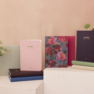 Peut inclure: Une collection d'agendas à couverture rigide dans diverses couleurs, notamment vert sauge, rose clair, bleu foncé, violet profond et un imprimé floral. Chaque agenda porte le texte doré twenty twenty seven sur la couverture avant.