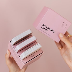 May include: A pink box set of journaling cards with the text "journaling cards" and "for reflection, inspiration & growth". The box is open, revealing several stacks of cards labeled "Inspiration" and "Reflection".