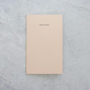 May include: A rectangular wellness tracker notebook with a solid light beige cover. The words wellness tracker are printed in small, black, lowercase sans-serif font centered near the top of the front cover. The notebook has a clean, flat design.