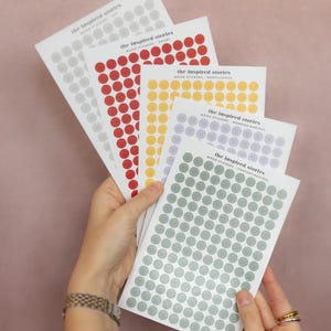 Pode incluir: Uma coleção de folhas de autocolantes de humor em várias cores, incluindo cinzento, vermelho, amarelo, roxo e verde. Cada folha apresenta autocolantes de carinhas sorridentes com diferentes expressões. O texto "the inspired stories" e as descrições de humor são visíveis.