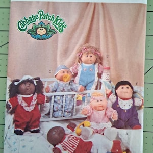 May include: Butterick 6509 sewing pattern envelope featuring Cabbage Patch Kids dolls. The cover displays six dolls in various outfits, including a red dress, blue overalls, and striped rompers, alongside a baby bottle and alphabet blocks.