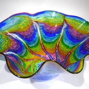 May include: A large, colourful glass bowl with a wavy, ruffled rim. The bowl is made of iridescent glass with shades of blue, green, yellow, pink, and white.