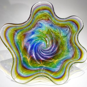 May include: A colourful glass bowl with a swirling pattern of blue, green, yellow, and purple. The bowl has a unique, organic shape with a wide, open mouth and a narrow base.