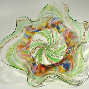 May include: A clear glass bowl with a wavy, star-shaped rim. The bowl is decorated with swirls of green, brown, and multi-coloured glass.