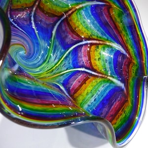 May include: A colourful glass bowl with a swirling pattern of blue, green, purple, and yellow. The bowl is made of thick glass and has a unique, organic shape.