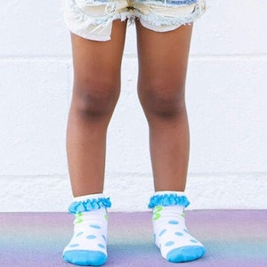 May include: A young person wearing a grey t-shirt with a rainbow and the word "hello" printed on it. They are also wearing denim shorts, round sunglasses, and blue and white polka dot socks.