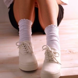 May include: White canvas low-top sneakers with white laces and a white frilly sock.