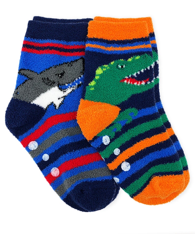 May include: A pair of blue, orange, green, and red striped fuzzy socks with a shark and dinosaur graphic. The socks have non-slip dots on the bottom.