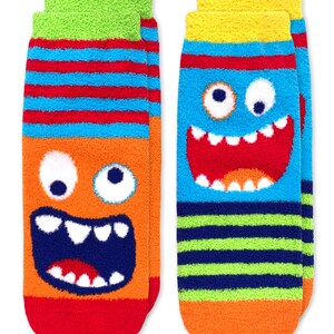 May include: Two pairs of fuzzy socks with monster faces. One pair has a blue monster face with a big smile and the other pair has an orange monster face with a big smile.