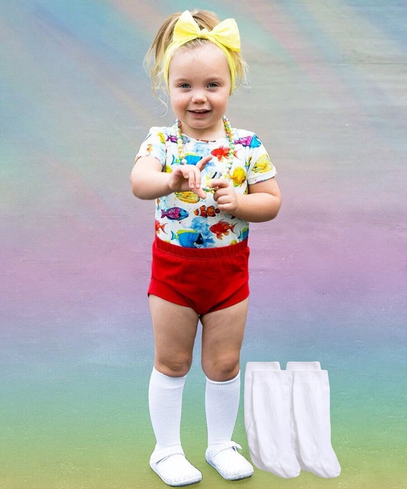 Puede incluir: Una ni&ntilde;a peque&ntilde;a con un mono corto rojo y blanco con estampado de peces de colores, calcetines blancos hasta la rodilla y zapatos blancos. Lleva una diadema amarilla con un lazo y un collar de cuentas. Tres pares de calcetines blancos hasta la rodilla est&aacute;n en primer plano.