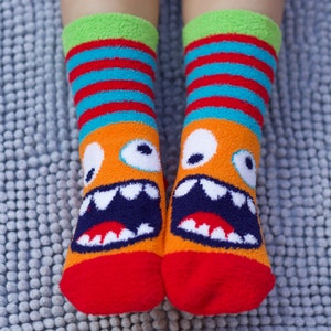 May include: A pair of red, orange, blue, and green fuzzy socks with a monster face design. The monster has white eyes, a white mouth with black teeth, and a red tongue.