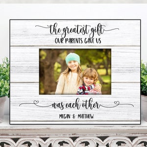 May include: White wooden picture frame with a black border. The frame has a photo of two children in it. The text on the frame reads "The greatest gift our parents gave us was each other Megan & Matthew".