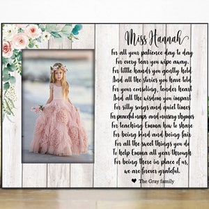 May include: A framed print with a floral design and a photo of a young girl in a pink dress. The print includes a poem thanking a teacher named Miss Hannah for her hard work and dedication. The poem reads: "For all your patience day to day, For every tear you wipe away. For little hands you gently hold, And all the stories you have told. For your consoling, tender heart, And all the wisdom you impart. For silly songs and quiet times, For peaceful naps and nursery rhymes. For teaching Emma how to share, For being kind and being fair. For all the sweet things you do, To help Emma all year through. For being there in place of us, we are forever grateful. The Gray family"