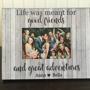 May include: A gray wooden picture frame with a white woodgrain pattern. The frame has a white mat and a 4x6 inch photo opening. The frame has the text "Life was meant for good friends and great adventures" with the names "Anna" and "Bella" below the text. The photo in the frame shows a group of people at a wedding.