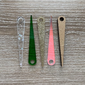 May include: Five decorative clock hands in different colors and textures. The hands are made of wood, glitter, and clear acrylic. The hands are all pointed and have a hole at the top for attaching to a clock mechanism.