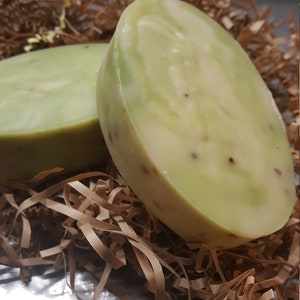 May include: Two green and white oval-shaped bars of soap with a speckled texture, sitting in a brown shredded paper nest.