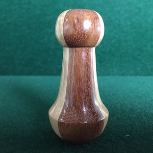 May include: A wooden bottle stopper with a rounded top and a bulbous base. The stopper is made from two different types of wood, creating a striped pattern.