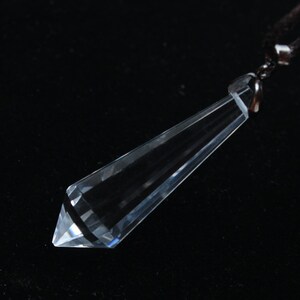 May include: A clear crystal pendant shaped like a long, pointed teardrop, hanging from a black cord.