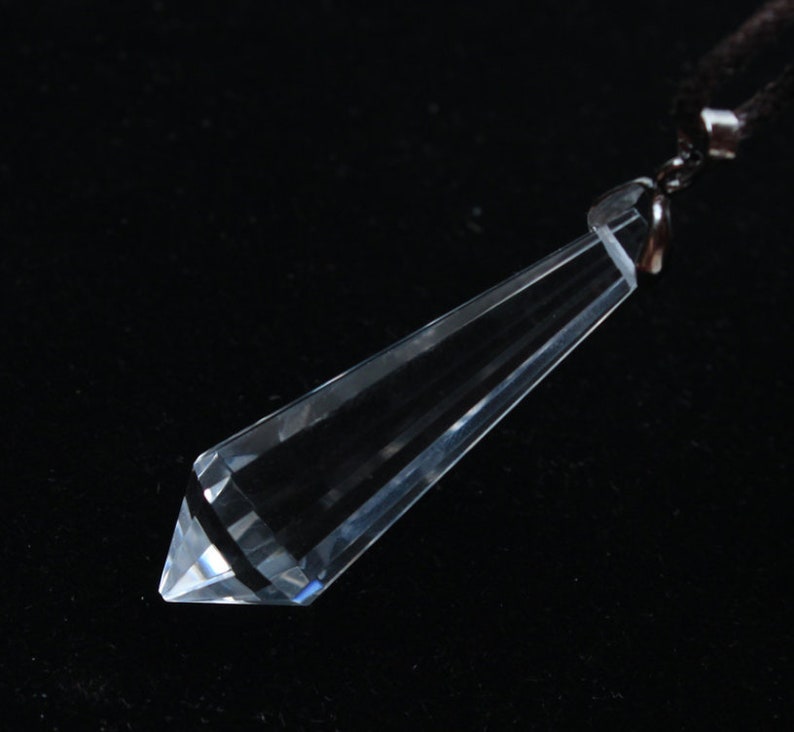 May include: A clear crystal pendant shaped like a long, pointed teardrop, hanging from a black cord.