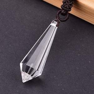 May include: A clear crystal point pendant with a black cord. The crystal is faceted and has a pointed tip.