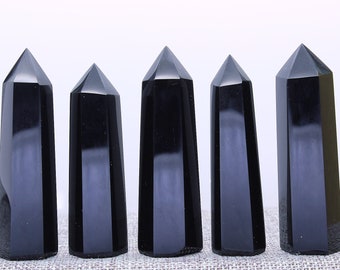 May include: Five black obsidian crystal points, each with a smooth, polished finish and a pointed tip. The crystals are arranged in a row on a textured surface.