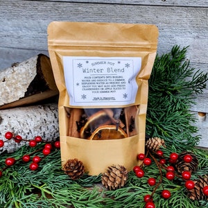 May include: A brown paper bag with a white label that reads "Simmer Pot Winter Blend". The label has snowflakes and instructions for using the contents. The bag contains a mix of dried orange slices, cinnamon sticks, cloves, and star anise.