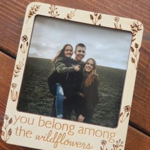 May include: A wooden photo frame with a floral design and the text "You belong among the wildflowers". The frame features a photo of three people smiling.