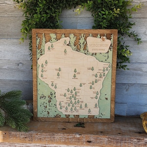 May include: A wooden map of Wisconsin state parks with the names of each park labeled. The map is framed in a brown wood frame and has a green background.