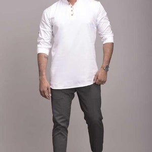 Pu&ograve; includere: Una camicia bianca a maniche lunghe con colletto alla coreana e tre bottoni, abbinata a pantaloni grigio scuro e mocassini neri. La camicia ha una vestibilit&agrave; morbida. I pantaloni sono a taglio slim. Le scarpe sono slip-on.